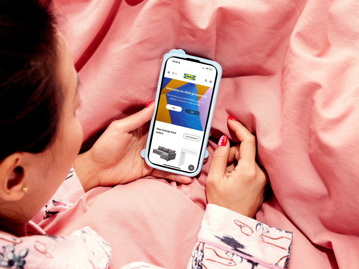 A person is holding a phone where the IKEA Marketplace website is visible, while lying on a pink blanket.