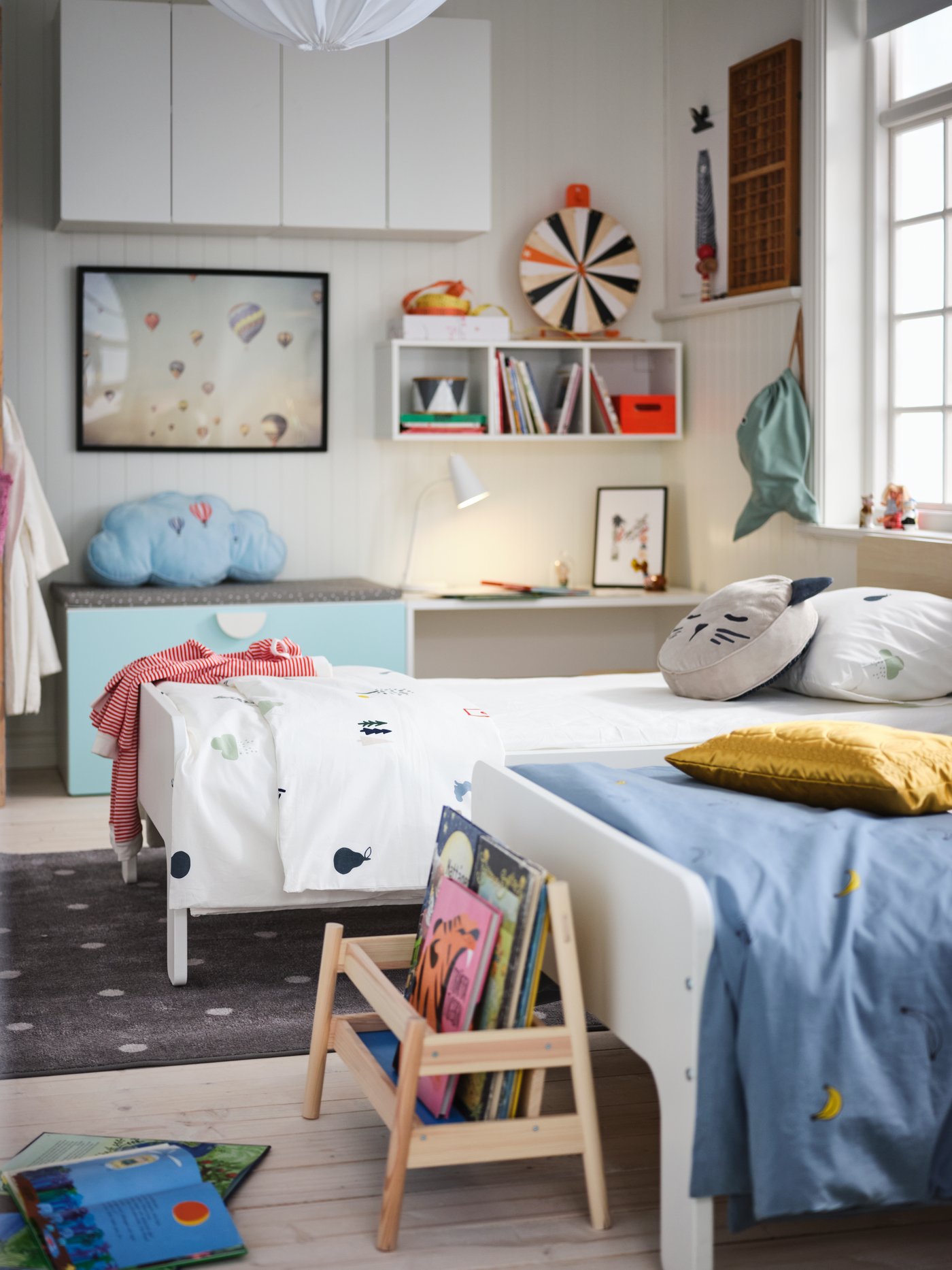 A children’s room with a pair of side-by-side, white SLÄKT extendable beds. Toys, decorations and storage line the walls.
