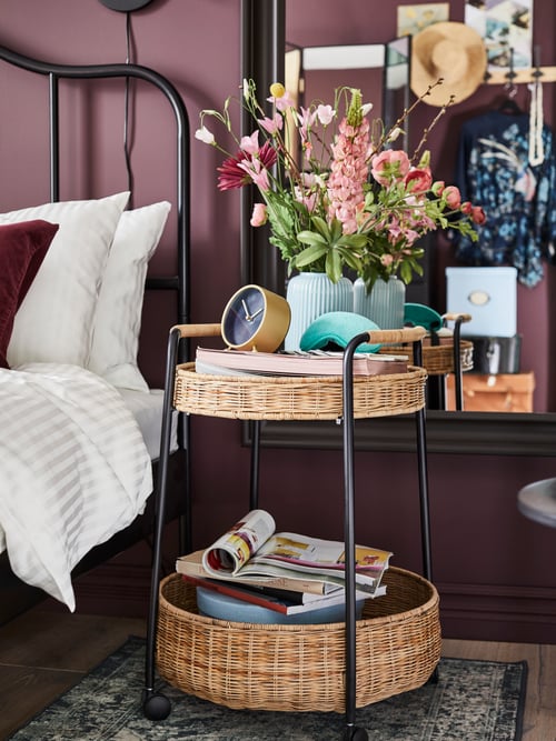 Bedroom with a pot with flowers, newspapers and table clock displayed on a trolley table with storage.