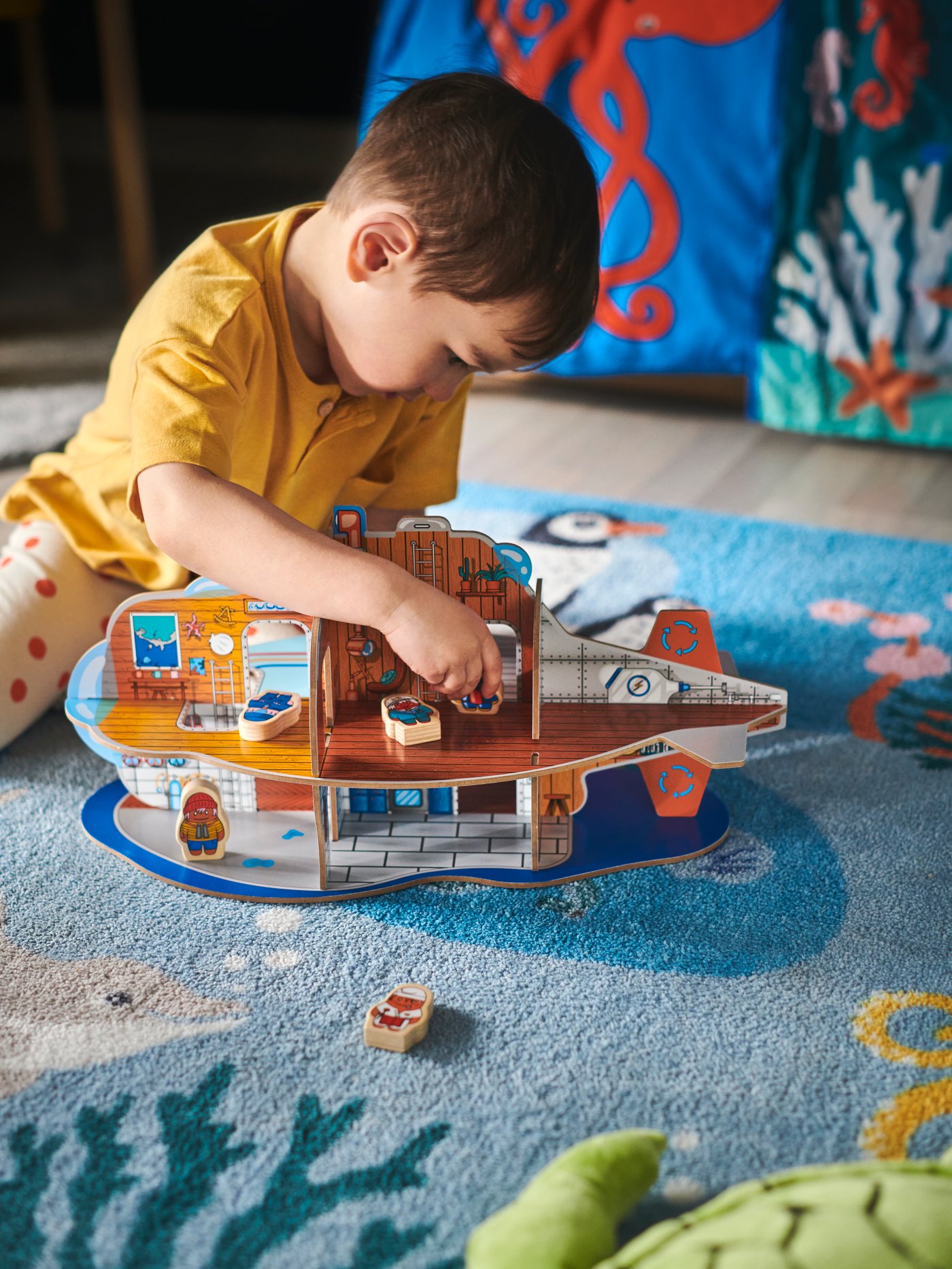 A young boy plays with a BLÅVINGAD submarine playset on a BLÅVINGAD ocean animal rug made from ocean-bound plastic.