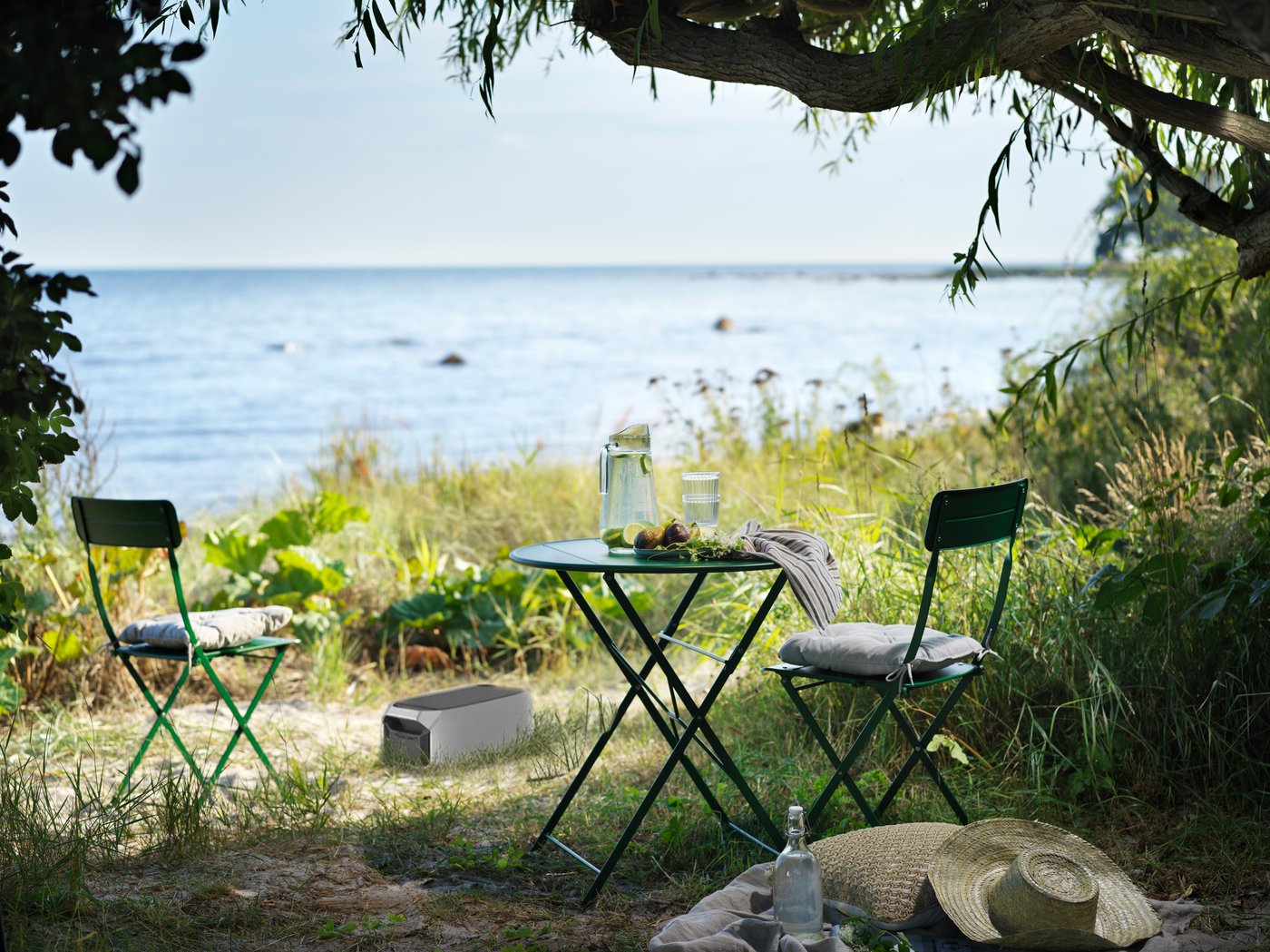 Ein Platz im Grünen mit Blick auf einen See, zwei Stühle ein Tisch und ein tragbarer Energiespeicher stehen auf einer Wiese.