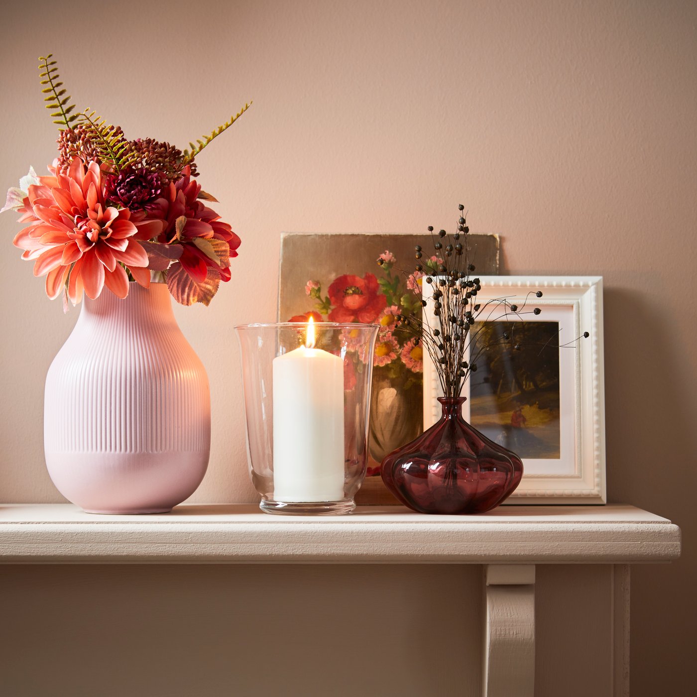 Artificial flowers in a vase, with a candle and photo frame.