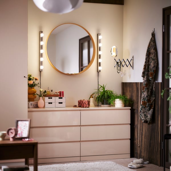 Two light orange MALM chests with 3 drawers side by side in the corner of a bedroom with a round mirror and lighting above.