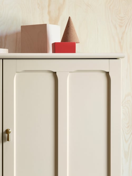 A close-up of the top right corner of a light beige LOMMARP cabinet with inset panels and champagne colour drop handles.