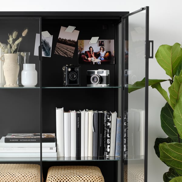 Schwarze IKEA Vitrine mit Büchern, Vintage-Kameras und Fotos – persönliche Aufbewahrung stilvoll präsentiert

