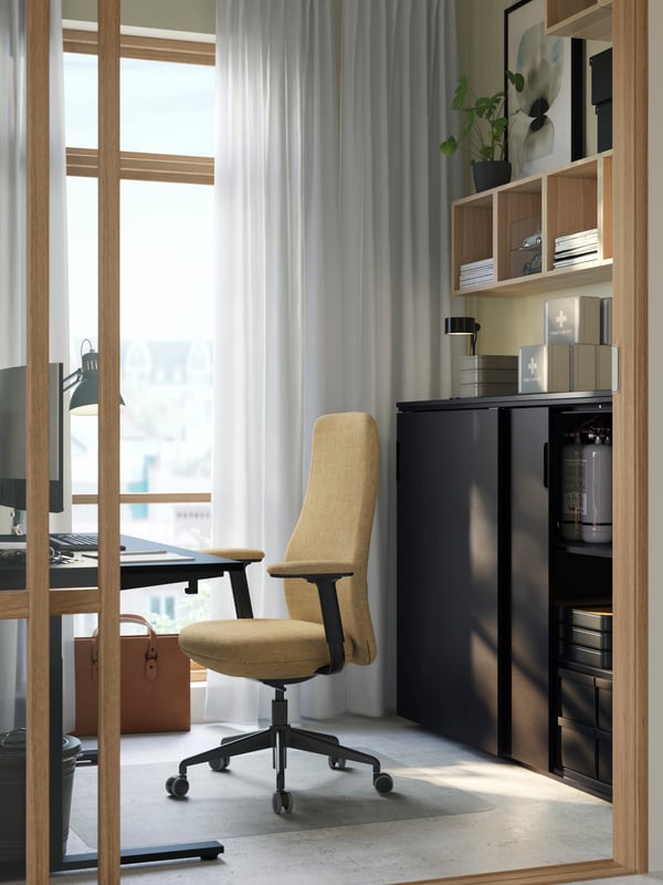 A small light-filled room with a workstation with a beige GRÖNFJÄLL chair and a black GALANT cabinet with sliding doors.