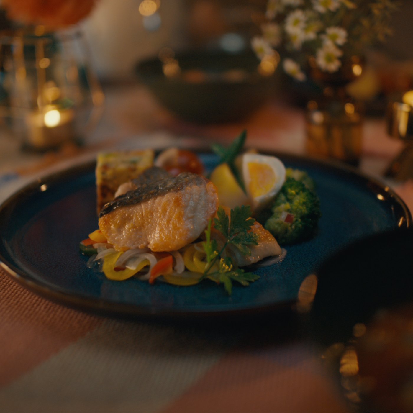 Fish dish with vegetables on a blue plate, flowers and candles on table