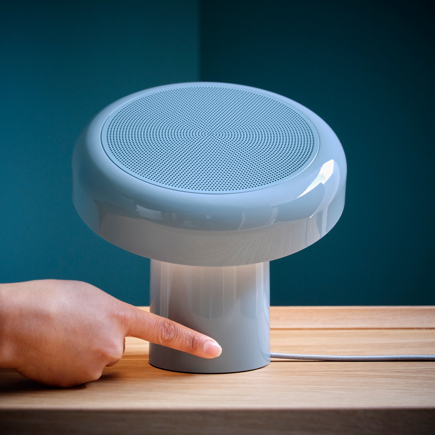 Una mano che sta accendendo una lampada/cassa Bluetooth® di colore azzurro BLOMPRAKT.