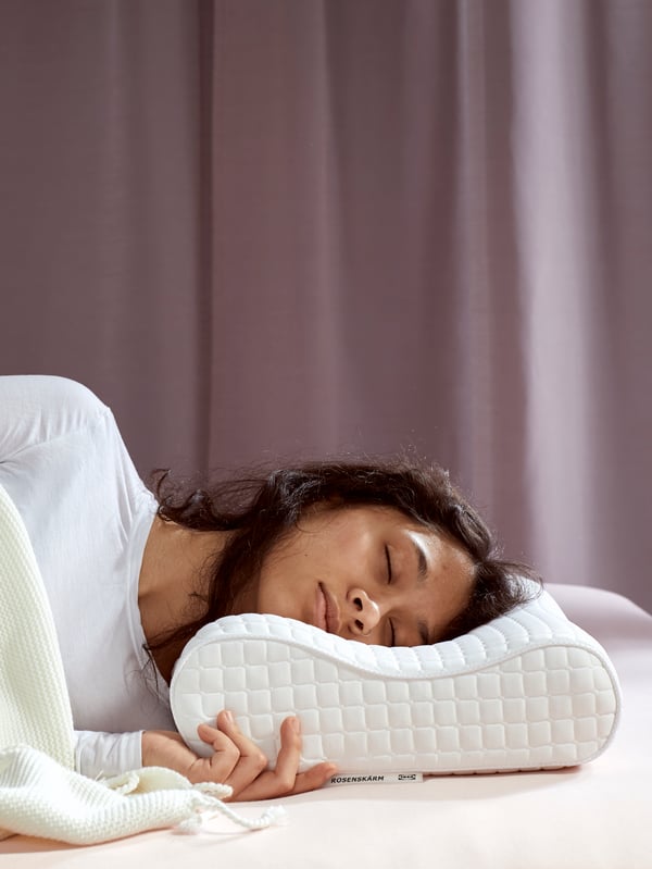 Henkilö nukkuu ergonomisen ROSENSKÄRM-tyynyn kanssa vaaleanpunaista taustaa vasten.