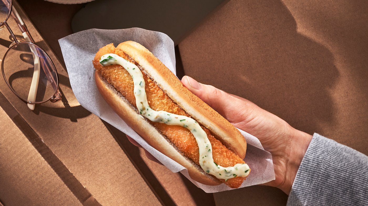 A hand holding a fish hot dog on top of cardboard boxes