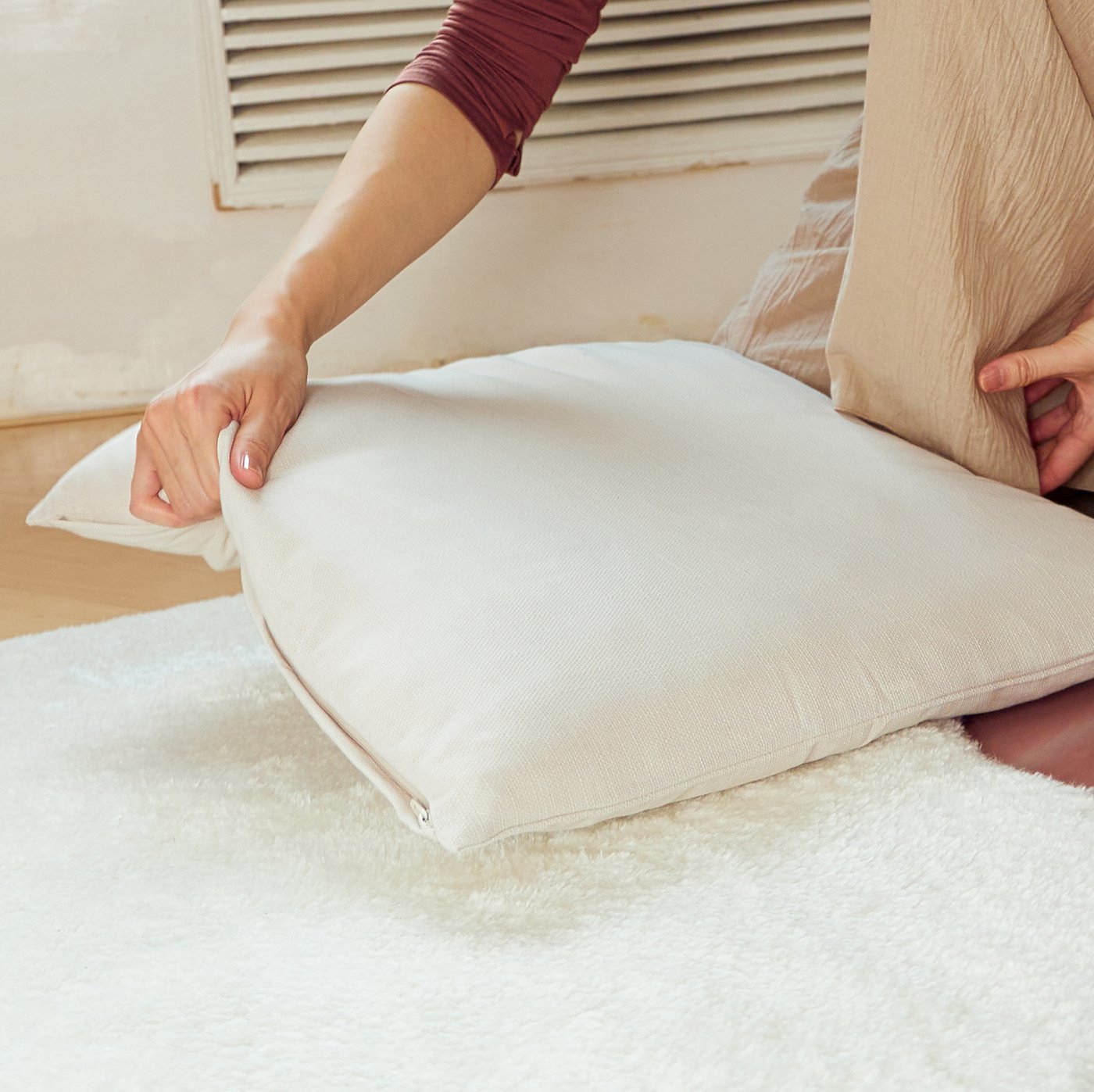 A woman places an INNER cushion with a MAJBRÄKEN cushion cover on a TOFTLUND rug on the floor.