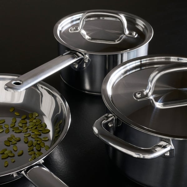 One large IKEA 365+ frying pan containing pumpkin seeds next to two smaller KEA 365+ saucepans with their lids on.