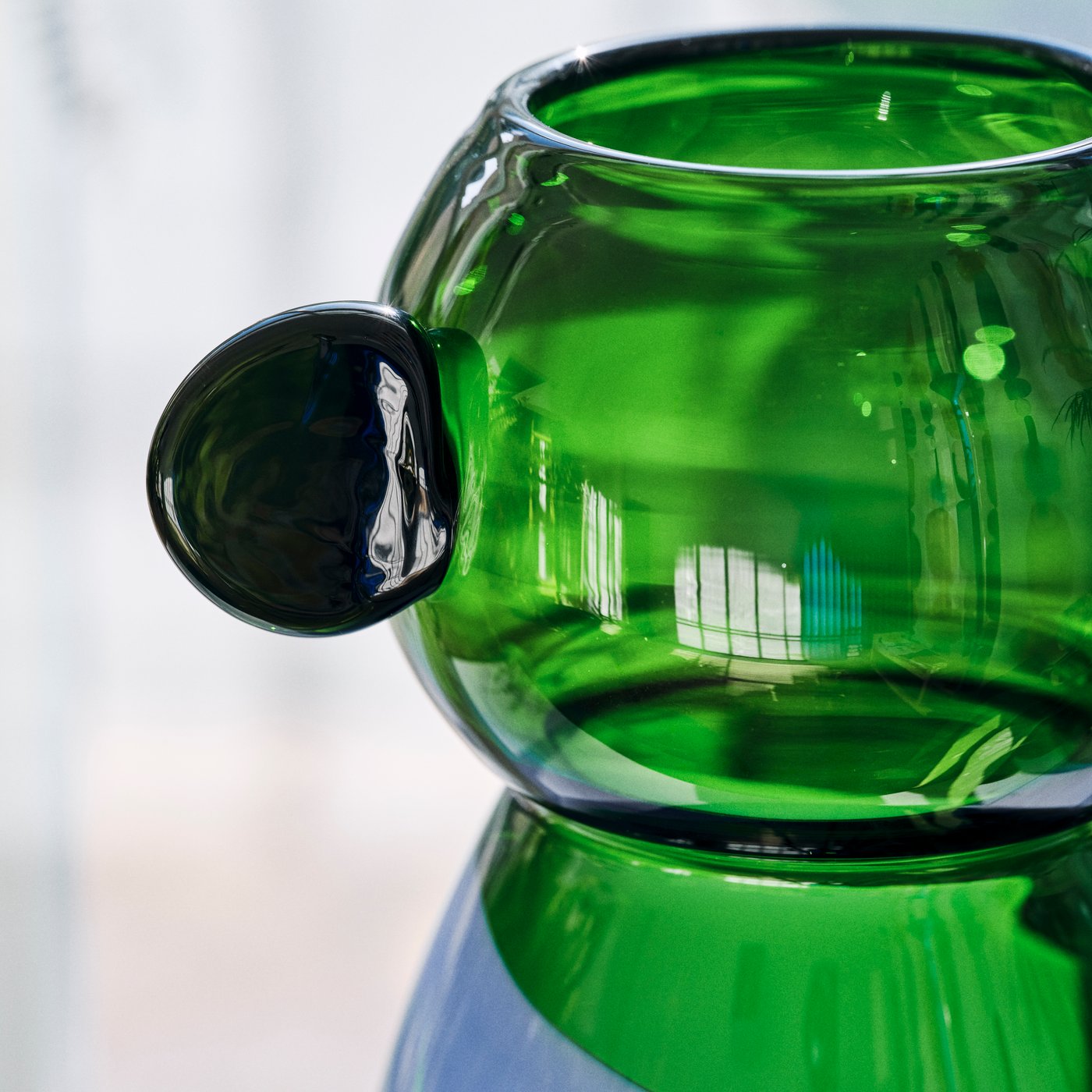 Vaso di vetro verde con superficie liscia e lucida e un manico rotondo e sporgente sul lato. I riflessi di luce gli conferiscono un carattere moderno ed elegante.