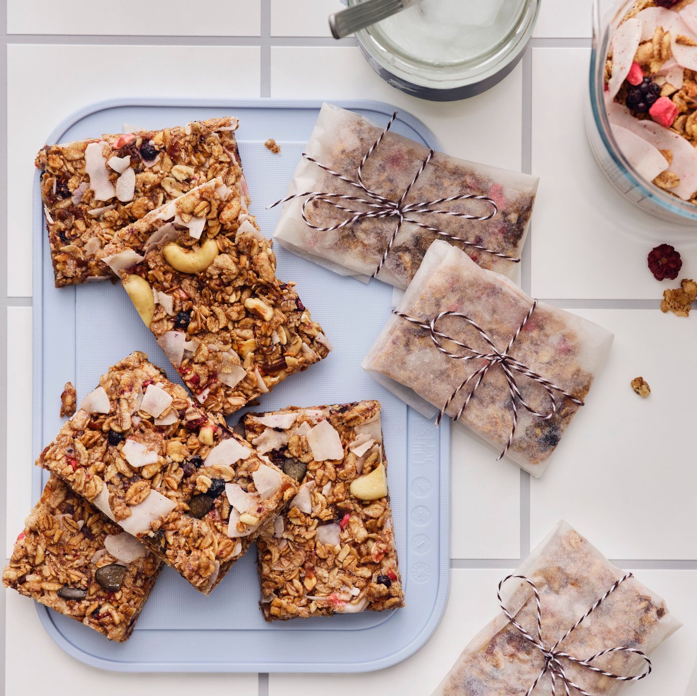 Home-made granola bars, cut into squares, some wrapped in baking paper, are placed on a grey chopping board on a table.
