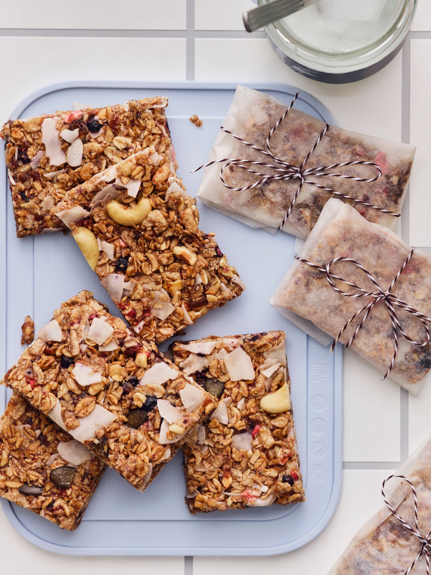 Barrette di granola fatte in casa, tagliate a quadratini, alcune avvolte in carta da forno, sono disposte su un tagliere grigio su un tavolo.
