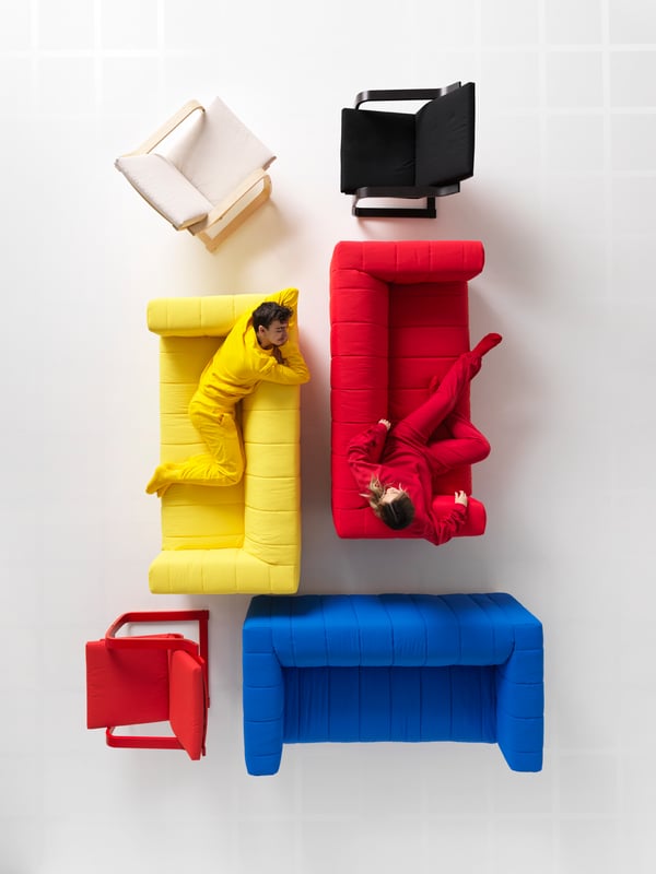 In a white room are KLIPPAN sofas and POÄNG low-back armchairs. Two people match the colours of the sofas they’re sitting in.