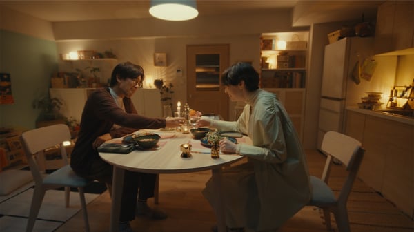 キャンドルの灯るダイニングで、2人が丸テーブルを囲み、温かい夕食とドリンクで乾杯している。