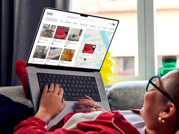 A person is lounging on a sofa, browsing IKEA Second-hand marketplace website on a laptop that displays various items for sale.
