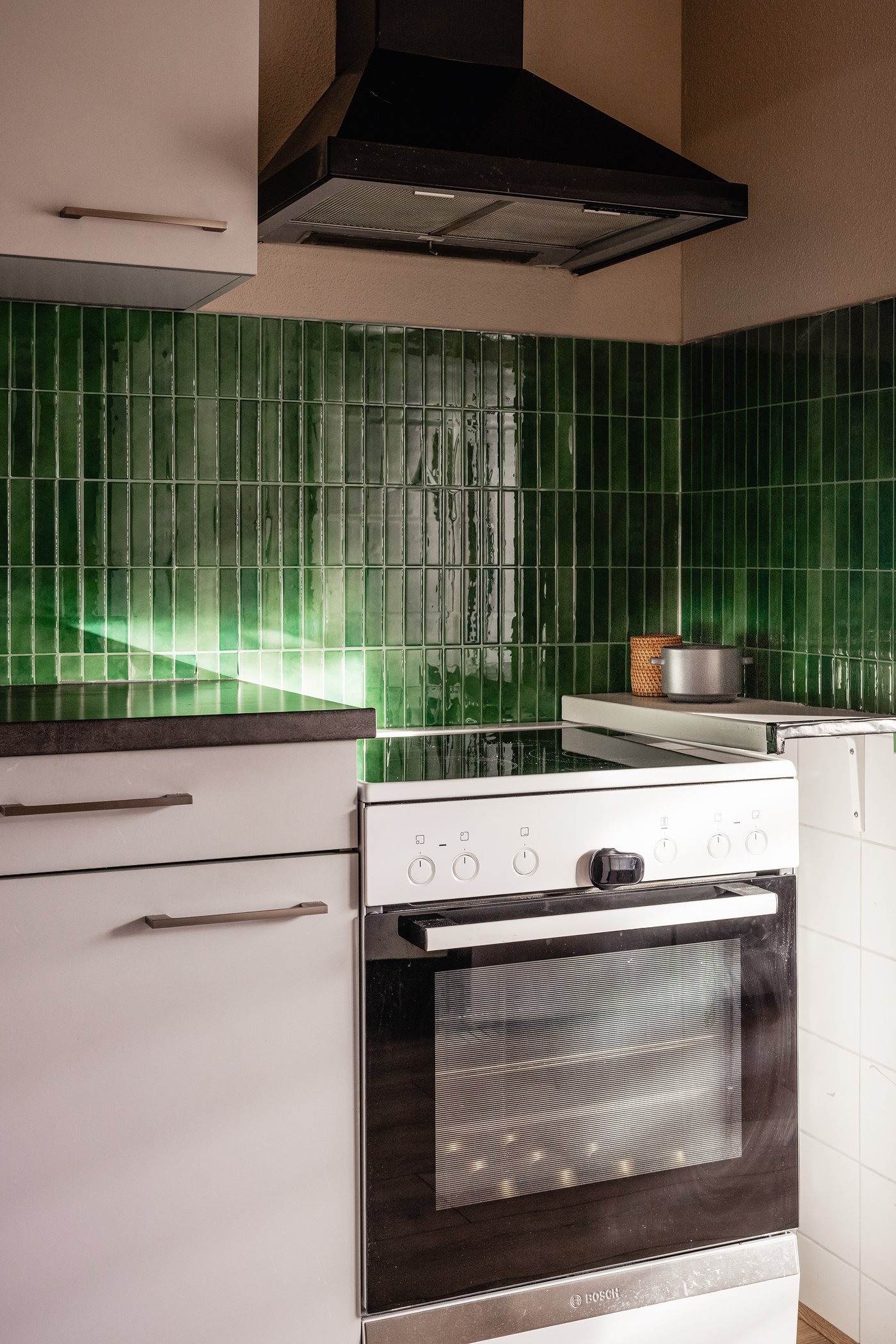 Een deel van een witte keuken met donker werkblad met daarnaast een oven. De keuken heeft donkergroene tegels aan de muur.