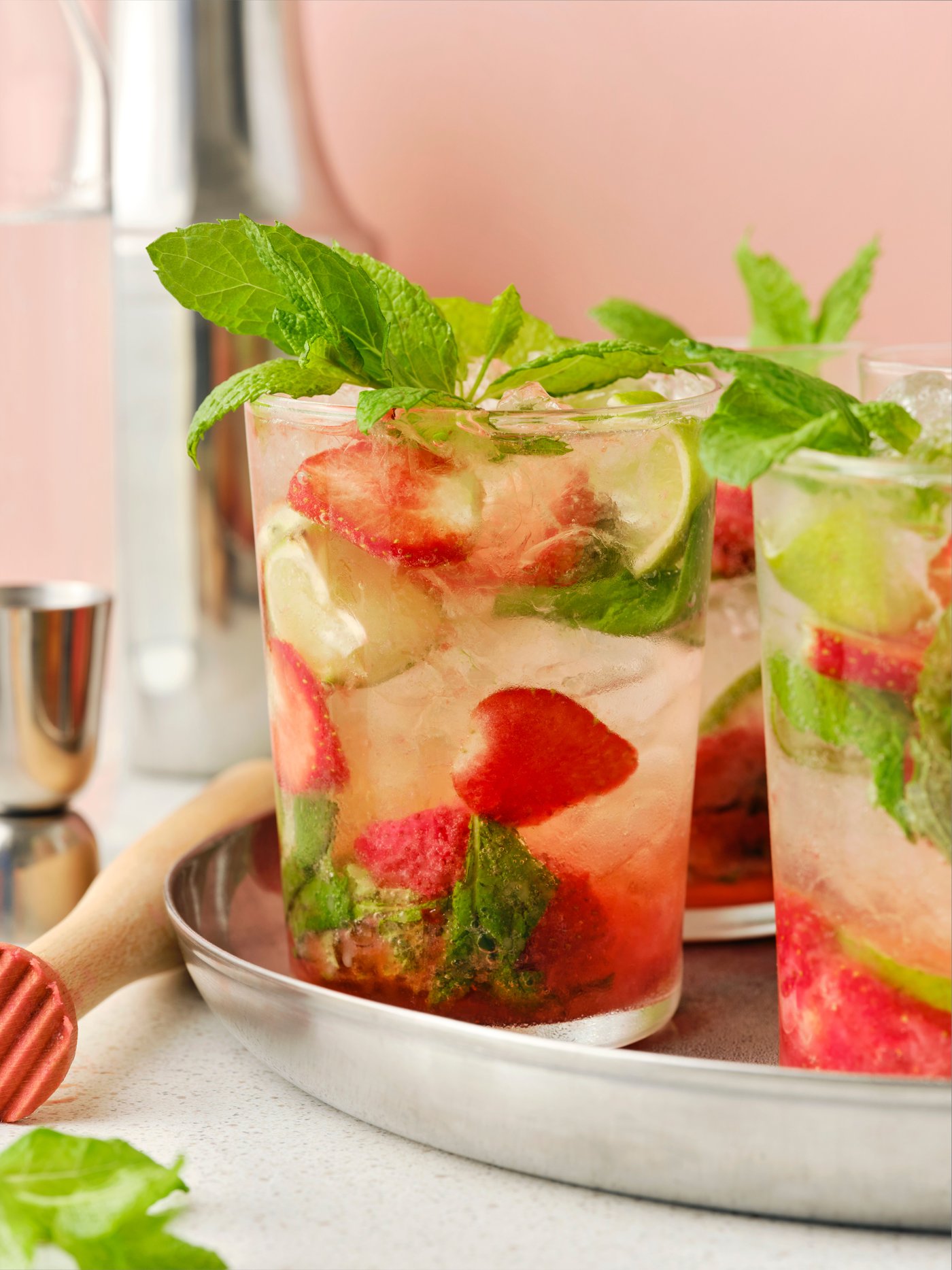 A glass filled with ISKUB lemon lime soft drink, strawberries and mint served on a silver tray.