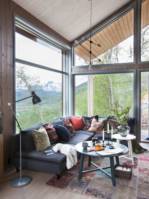 Koselig stue med en sofa full av puter. Fine høstfarger utenfor.