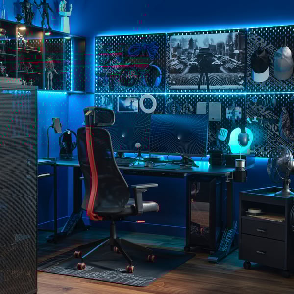 IKEA MATCHSPEL Bomstad black gaming chair in the gaming room lit with blue light, furnished with two monitors, desk, cabinetry, peg boards, and a variety of gaming accessories.