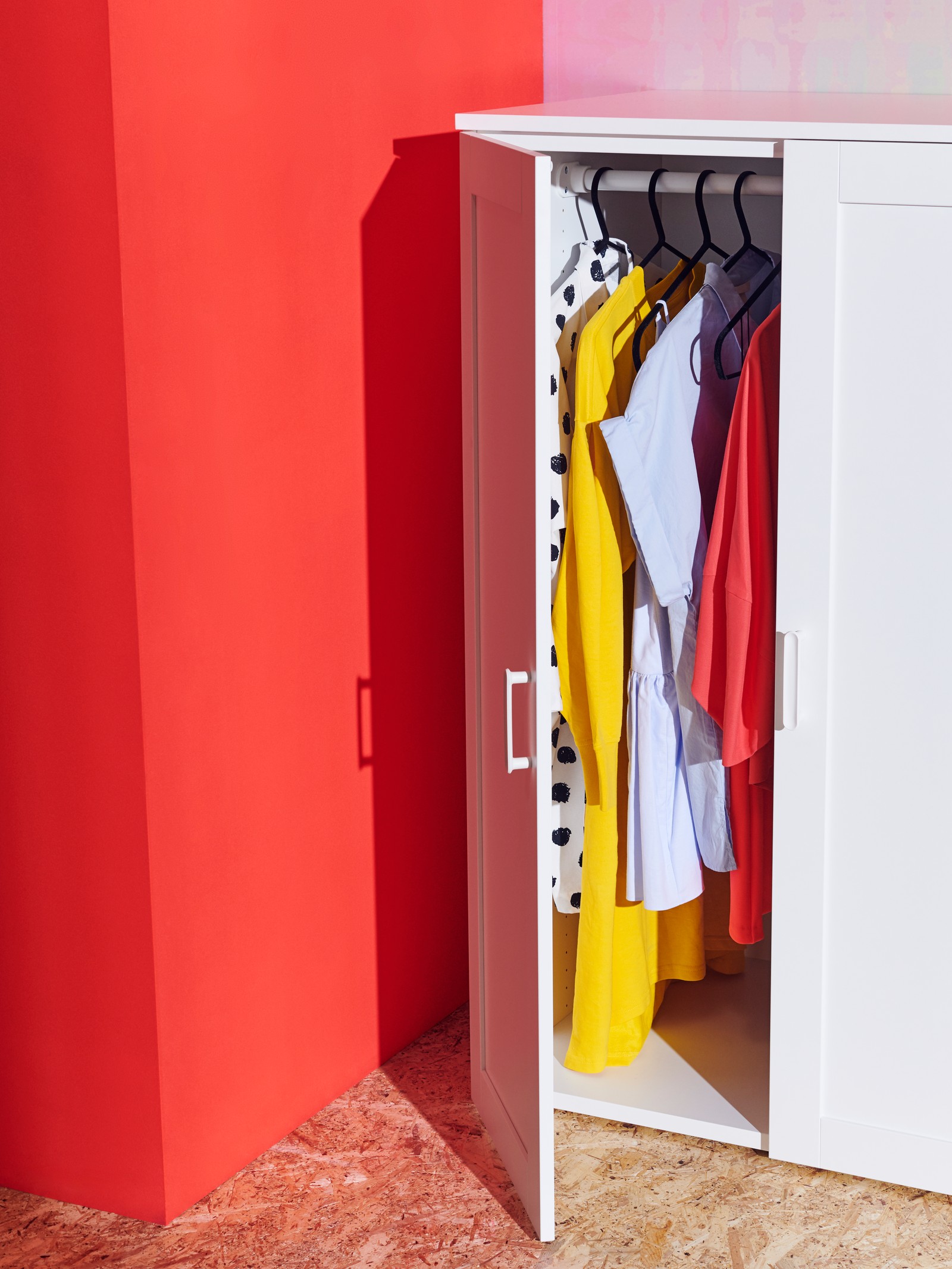 Crvena pozadina i beli ormarić u prvom planu u kom su stvari.