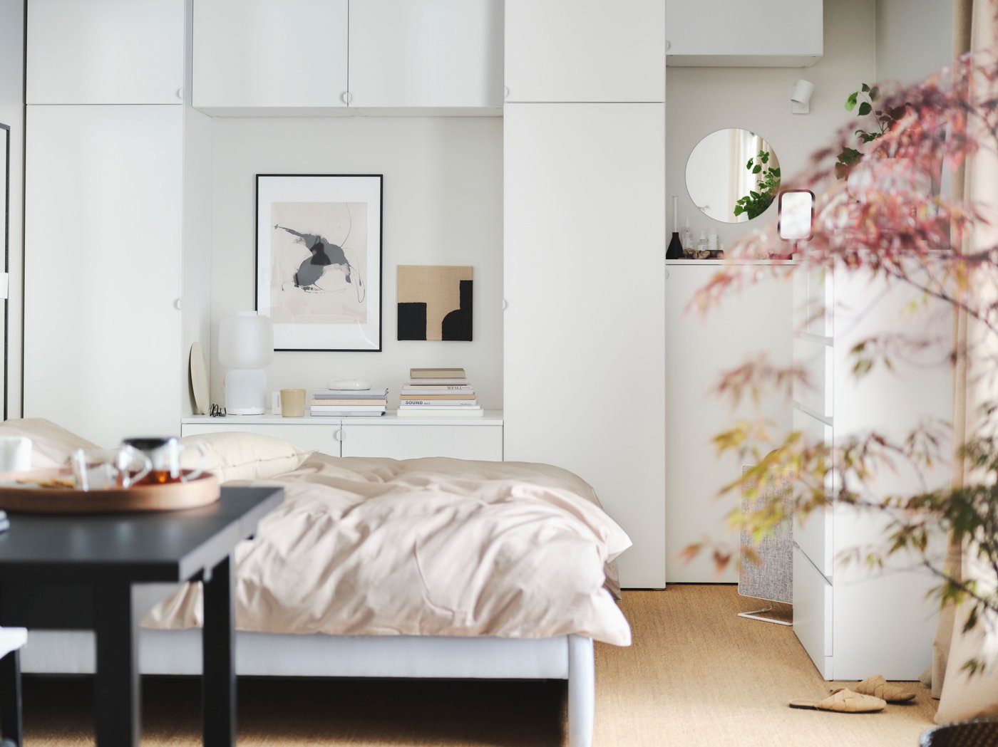 Klidná ložnice s šedou postelí GLADSTAD, dřevěným stolem, dynamicky působící šedou šatní skříní a kulatými stropními lampami.