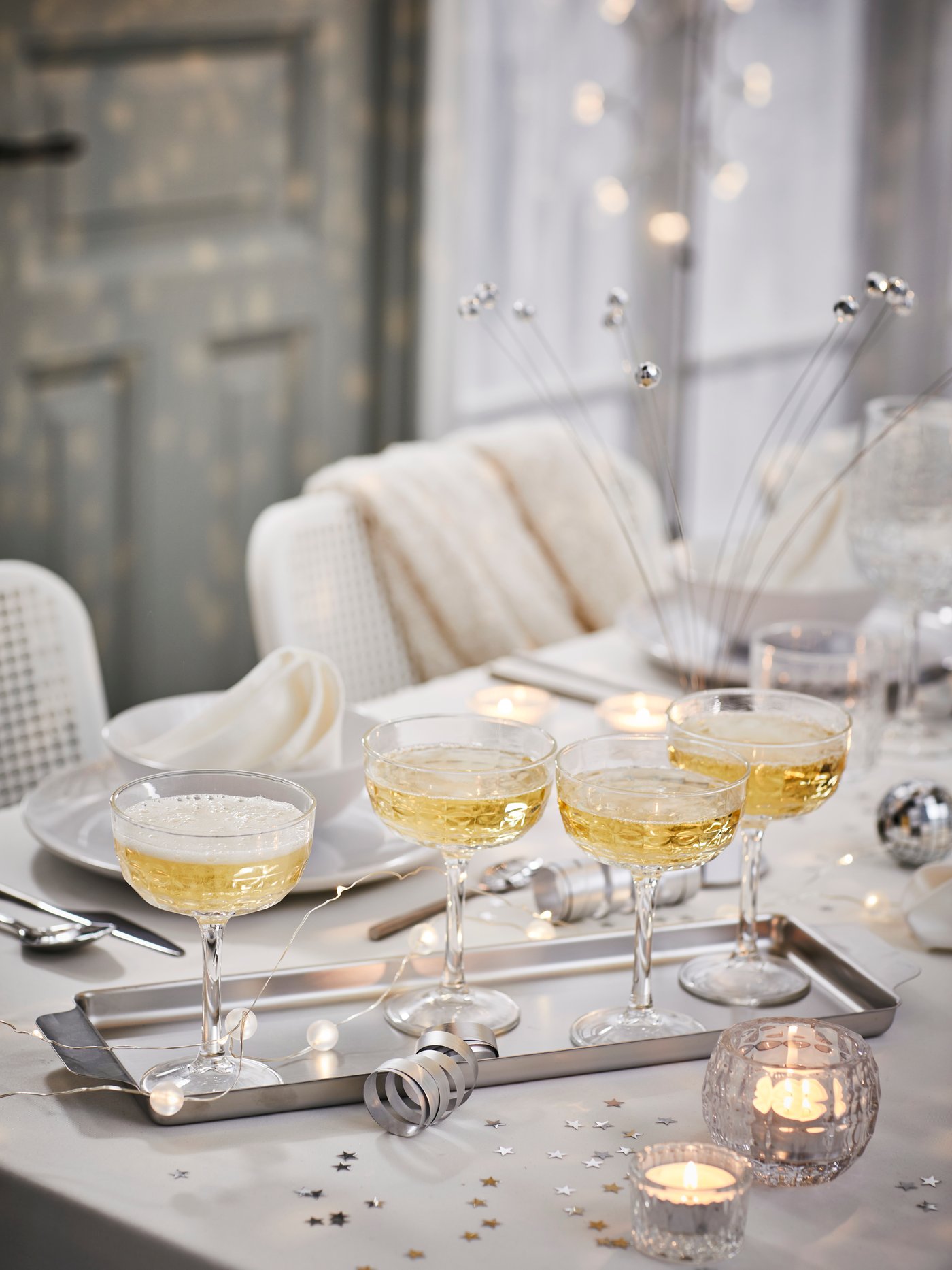 Ein weißer GODMIDDAG Teller steht auf einem weißen Tisch mit viel Deko. An der Seite stehen graue Stühle.