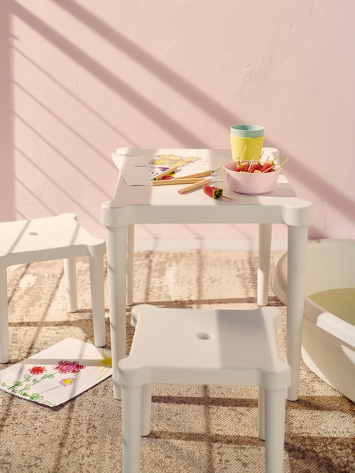 A white UTTER children’s table with two stools creates an activity corner for the kids on a balcony with light pink walls.