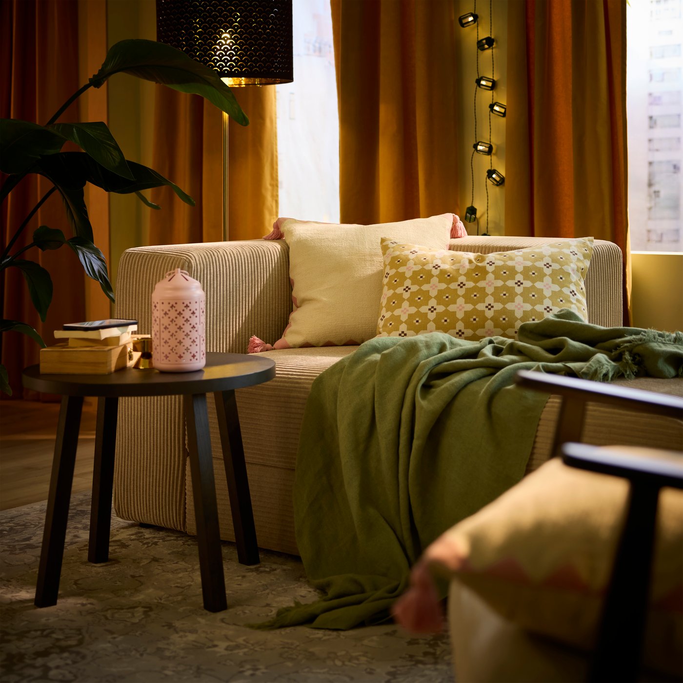 Two multicoloured GOKVÄLLÅ cushion covers rest on a sofa, accompanied by a throw, in a cosy living room.