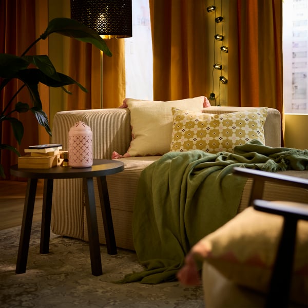 Deux housses de coussin GOKVÄLLÅ multicolores et un jeté sur un canapé, dans un salon chaleureux.