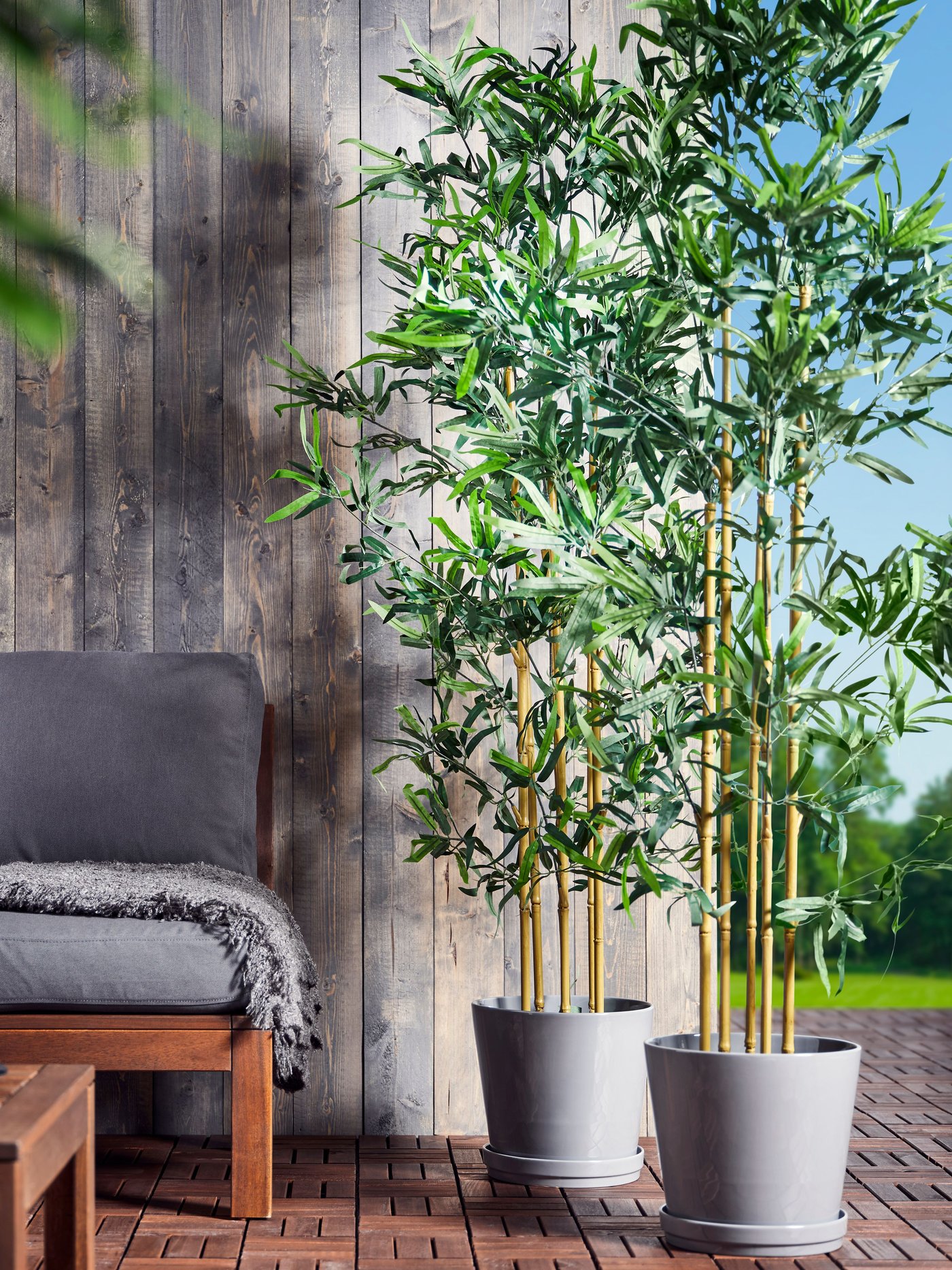 Two outdoor pots beside an outdoor furniture with tall plants in them.