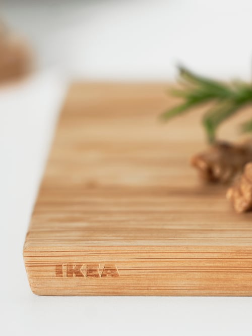 Gros plan dans une cuisine d’une planche à découper beige en bambou avec des bords inclinés faciles à tenir, placée sur une surface blanche.