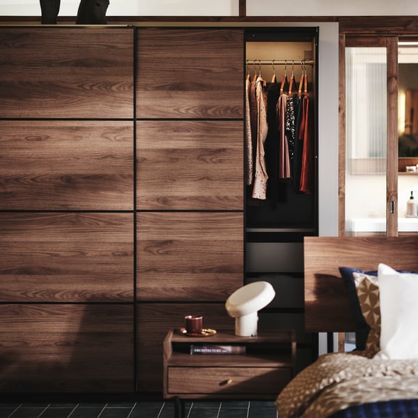 A bedroom with RÅDMANSÖ chest of drawers and bedside table plus PAX MEHAMN wardrobe in the background. All in dark wood.