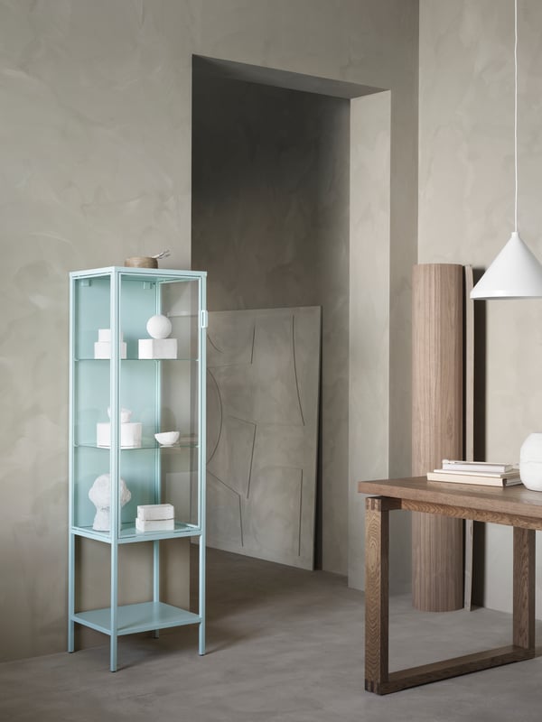 The turquoise RUDSTA glass-door cabinet filled with white ornaments in a minimal, neutral space.