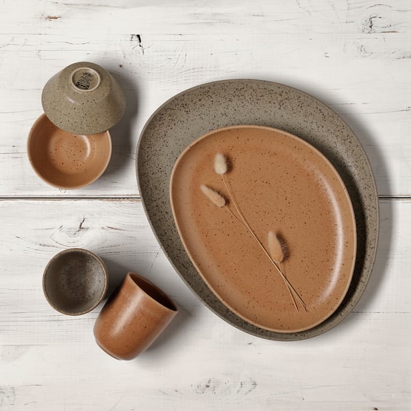 Brown and grey GRÅRÄV dinner plates, bowls, and coffee mugs on a light wooden surface.