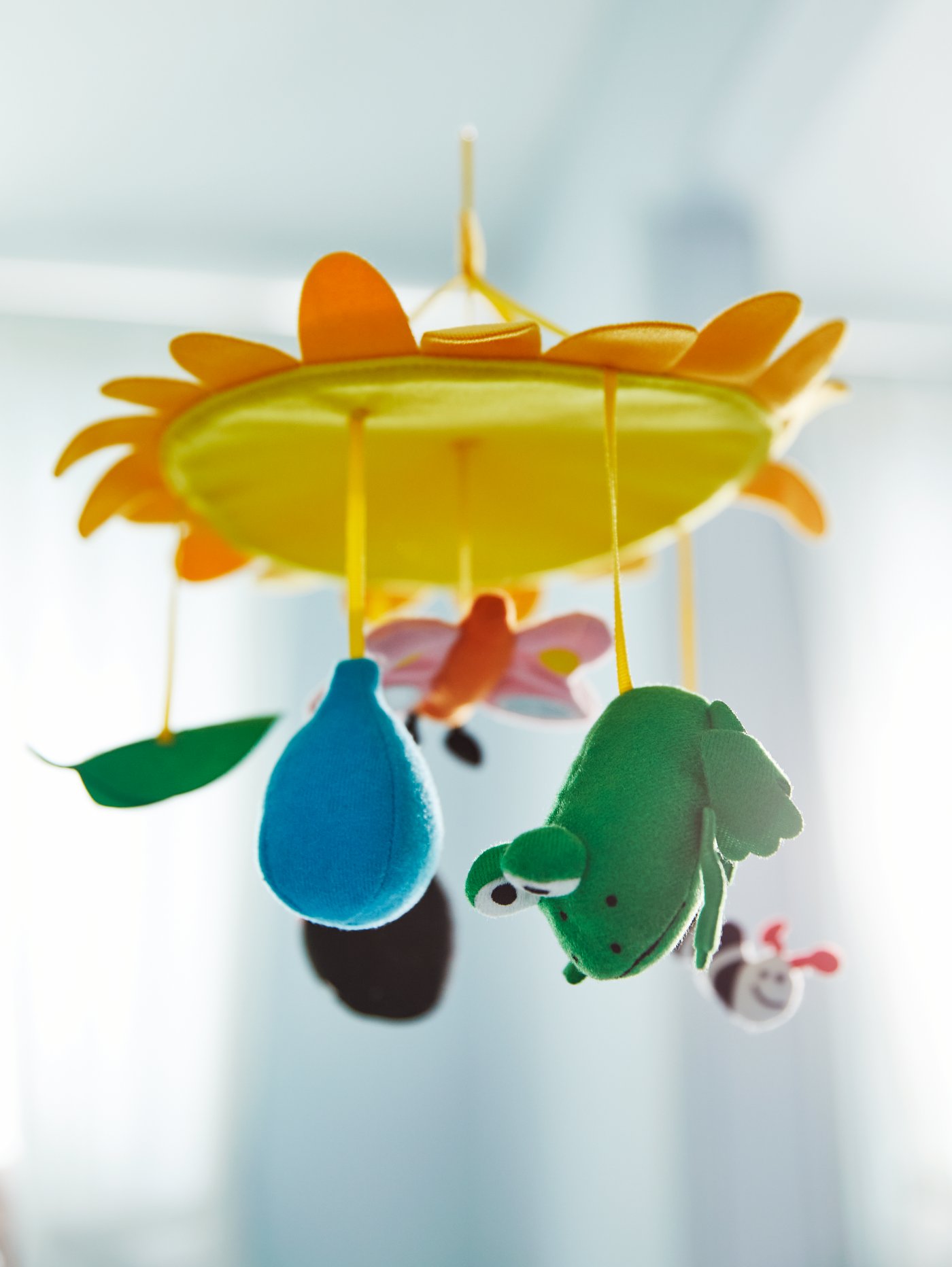 Un mobile jaune KLAPPA avec des animaux, un papillon et des formes de couleurs diverses.