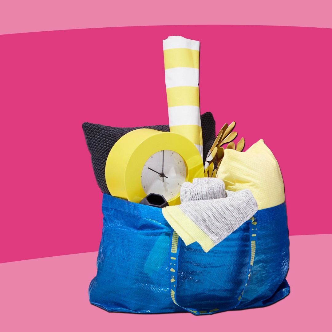 Vaaleanpunaisella taustalla on sininen IKEA-kassi, jossa onerilaisia keltaisia esineitä.