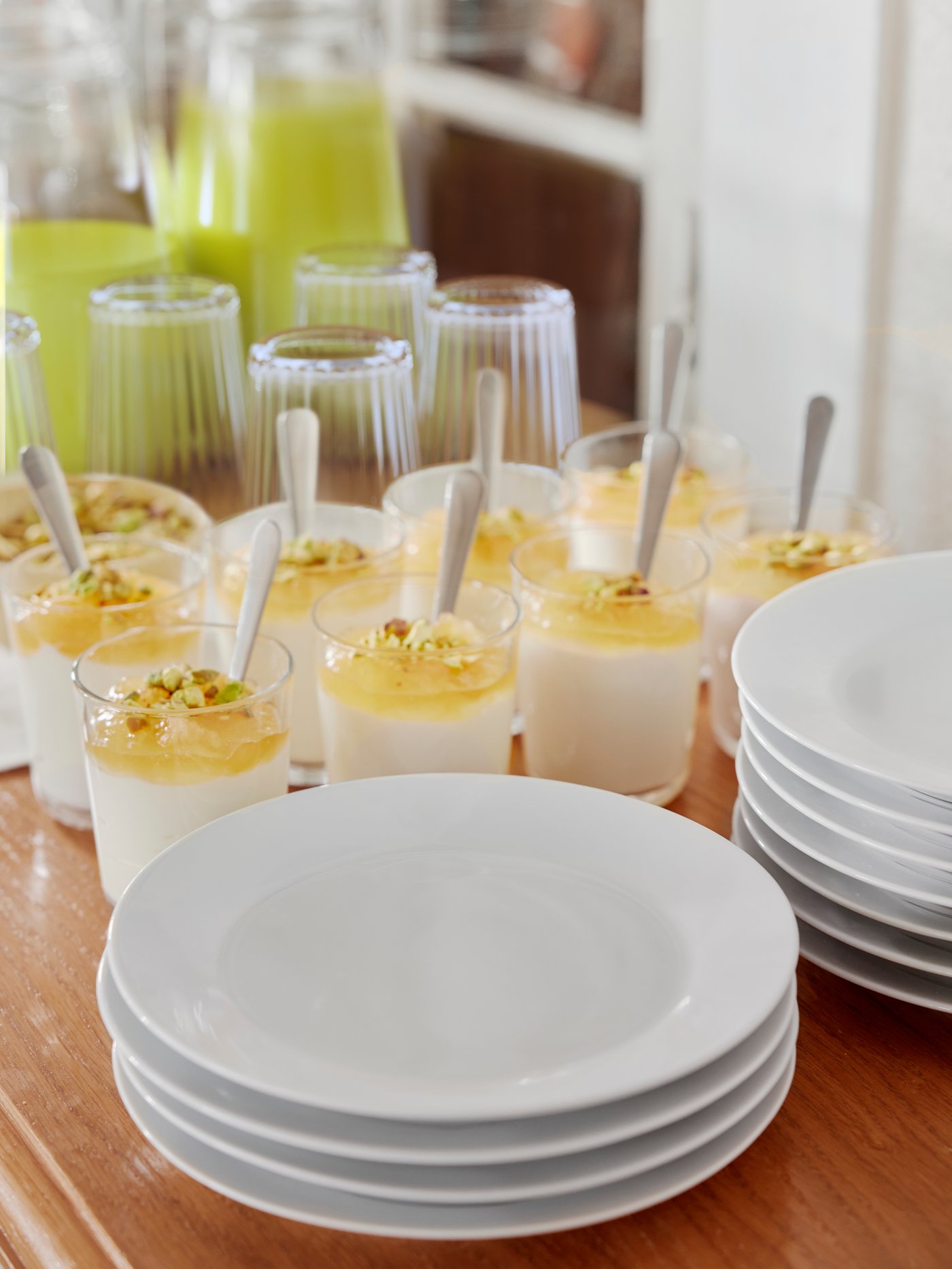 A sideboard with carafes with drink, treats served in IKEA 365+ glasses with DRAGON spoons, and stacks of IKEA 365+ plates.