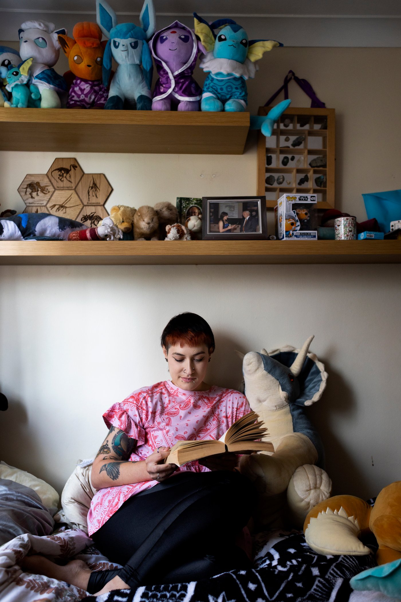 Woman sitting on her bed, surrounded by soft toys, reading a big book.