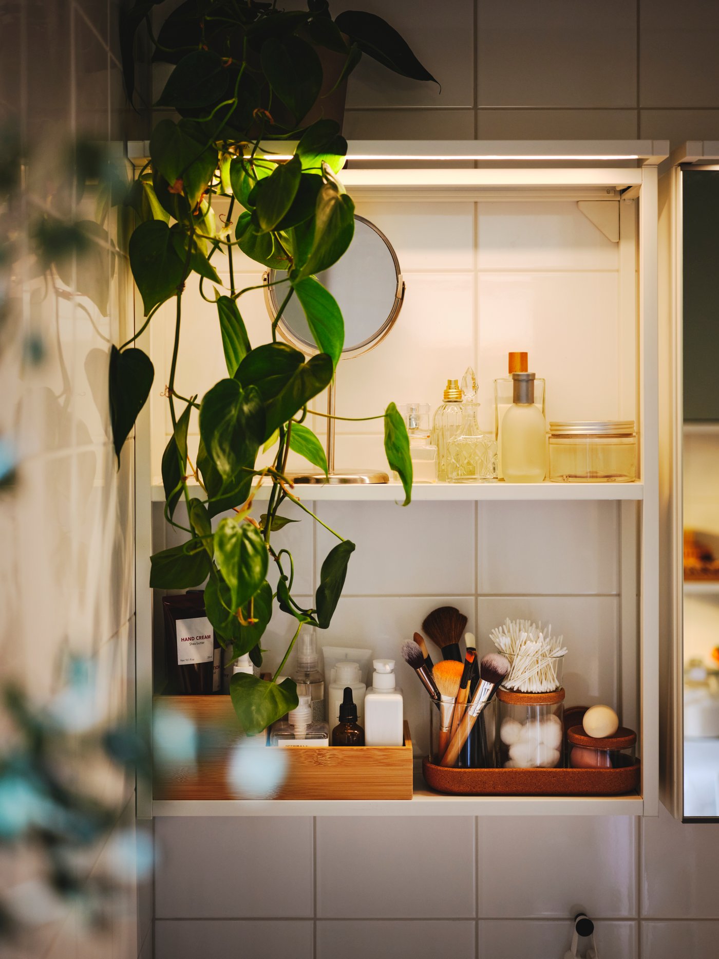 Toaletní potřeby v sadě 5 dóz s víky SAXBORGA a s podnosem na bílém rámu se 2 policemi ENHET, který je připevněný na zdi.