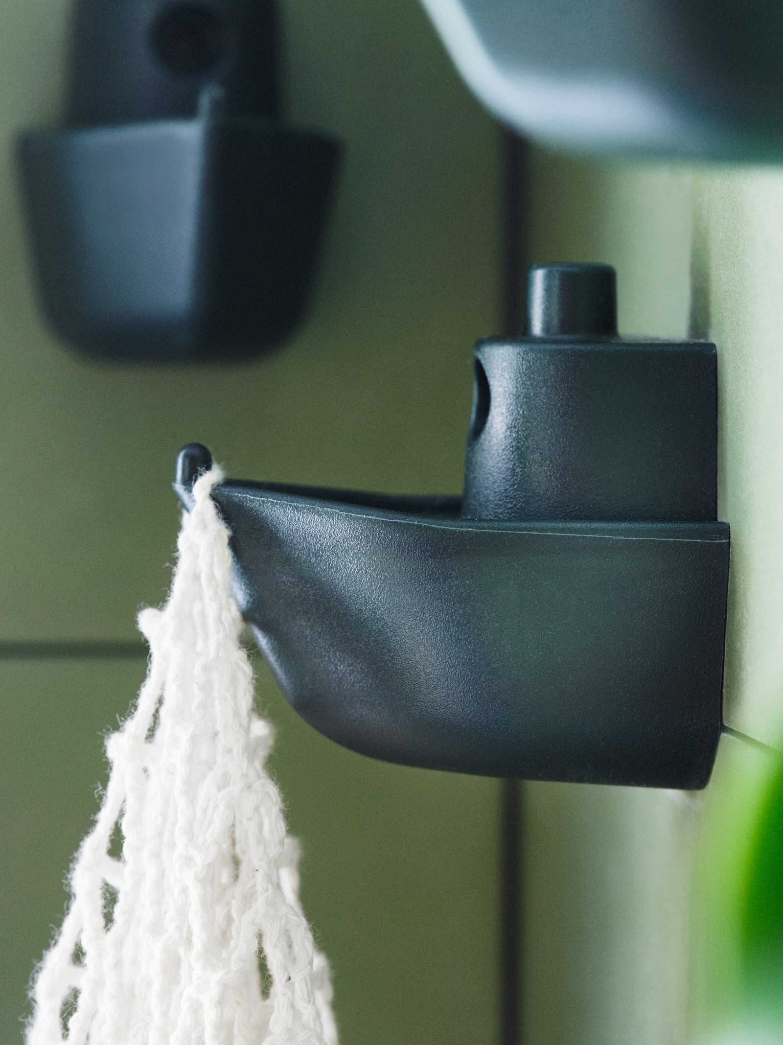 Trzy haki ścienne KNOPARE zamontowane na różnych wysokościach, a na jednym z nich wisi biała torebka z makramy.