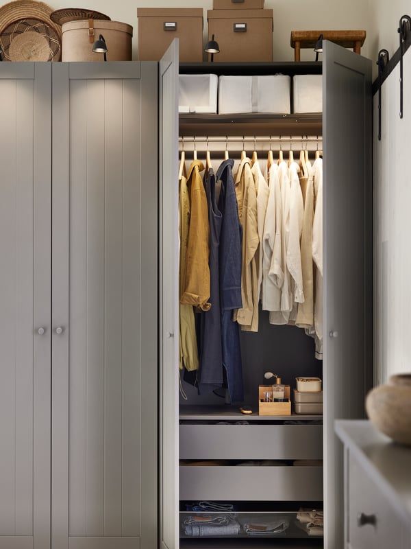 A dark grey/grey PAX/GULLABERG wardrobe combination with two doors open showing hanging clothes and storage boxes on shelves.