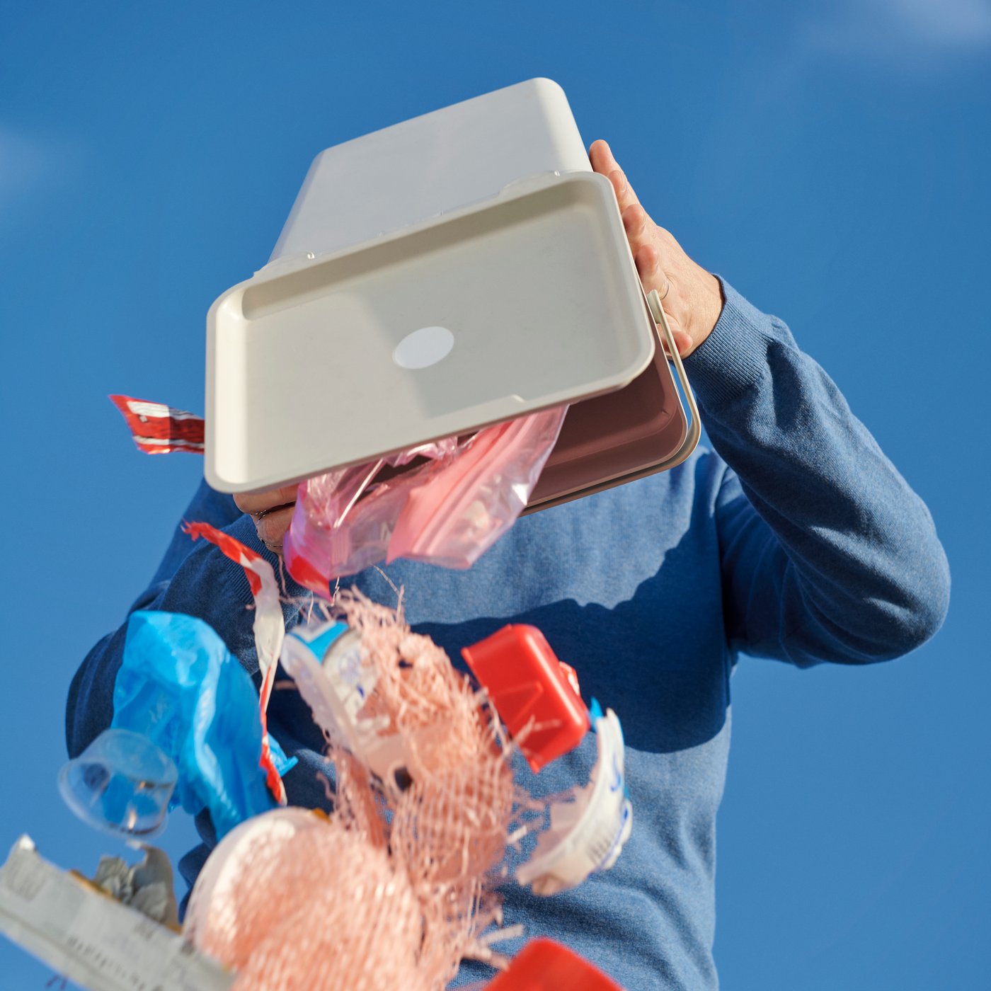 A person holding an upside-down HÅLLBAR bin while throwing out rubbish.