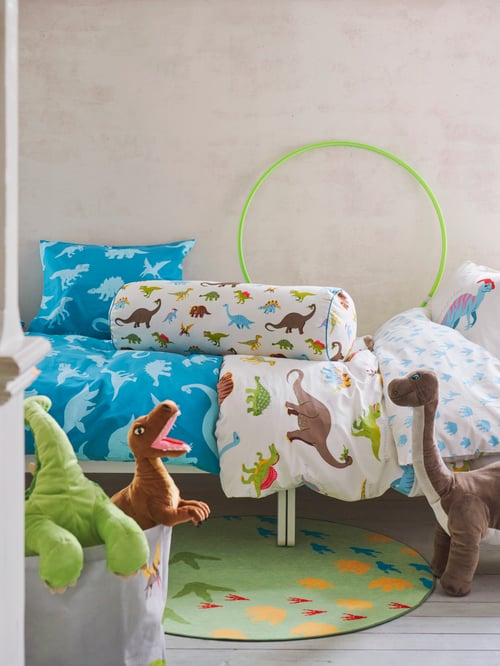 Deux garçons couchés, la tête sur un coussin JÄTTELIK dans un lit réalisé avec la série textile JÄTTELIK à motifs de dinosaures.