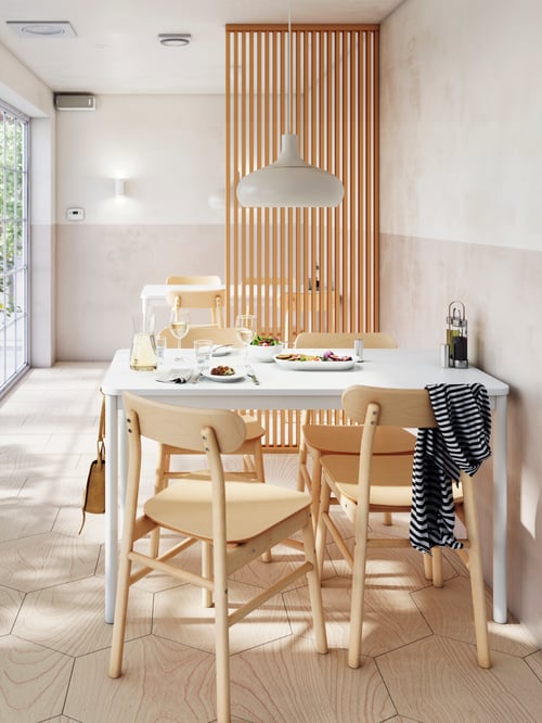 A birch RÖNNINGE table and four matching chairs by a wall in a bar with a pendant lamp above and plates of food on top.