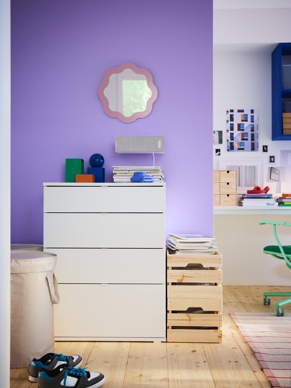 White VIHALS chest of drawers in front of a bright purple wall, with wooden boxes next to it and a round mirror on the wall.