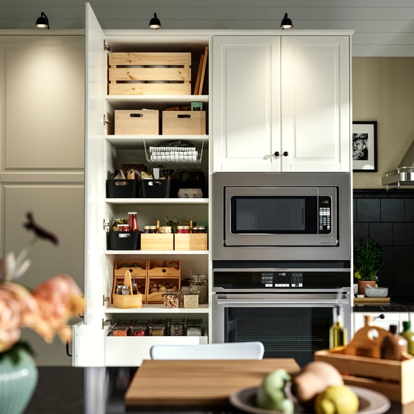 A modern kitchen with a stainless steel oven and microwave, a neatly organised cupboard with UPPDATERA storage boxes.