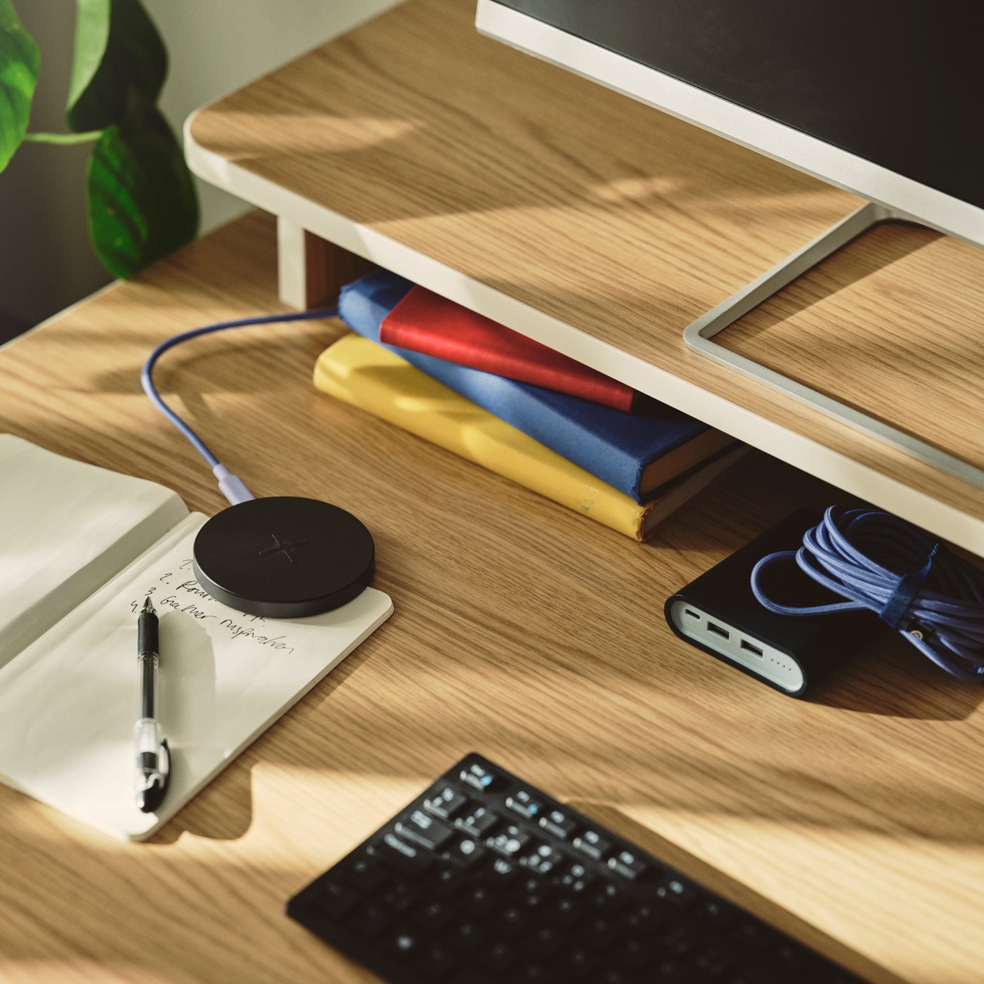 A close-up of a black LIVBOJ wireless charger on a desk, with a notebook, pen, and colourful books nearby.